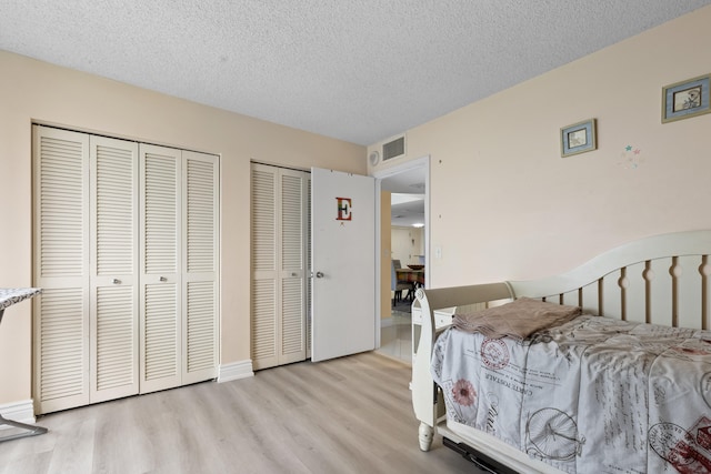 bedroom with two closets, light hardwood / wood-style floors, and a textured ceiling