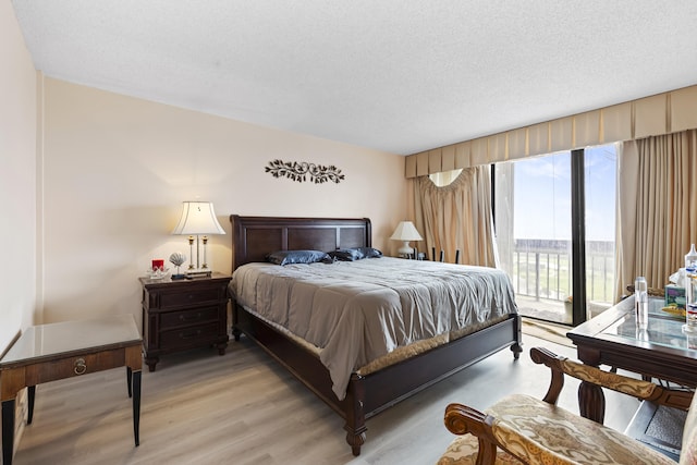 bedroom featuring access to exterior, light hardwood / wood-style floors, and a textured ceiling