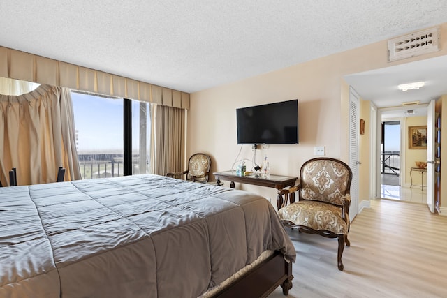 bedroom featuring access to outside, a textured ceiling, and light hardwood / wood-style flooring