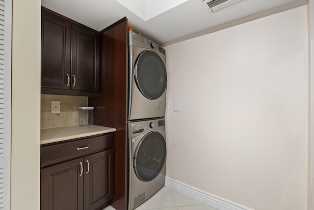 clothes washing area featuring cabinets, stacked washer and clothes dryer, and light tile patterned floors