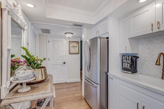 kitchen with sink, white cabinets, stainless steel fridge, decorative backsplash, and crown molding