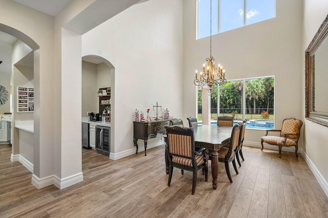 dining space featuring light hardwood / wood-style floors, a chandelier, beverage cooler, and a towering ceiling