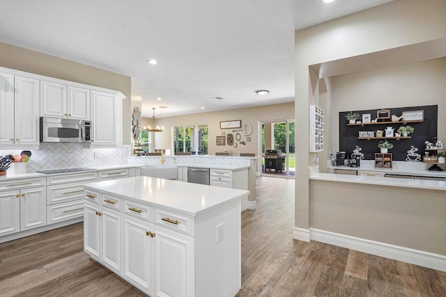 kitchen with kitchen peninsula, appliances with stainless steel finishes, decorative backsplash, hanging light fixtures, and a kitchen island