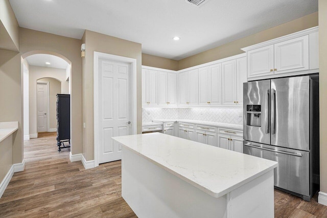 kitchen with white cabinetry, stainless steel fridge, decorative backsplash, a kitchen island, and light stone counters