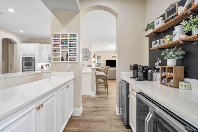 kitchen featuring white cabinetry, beverage cooler, light hardwood / wood-style flooring, and light stone counters