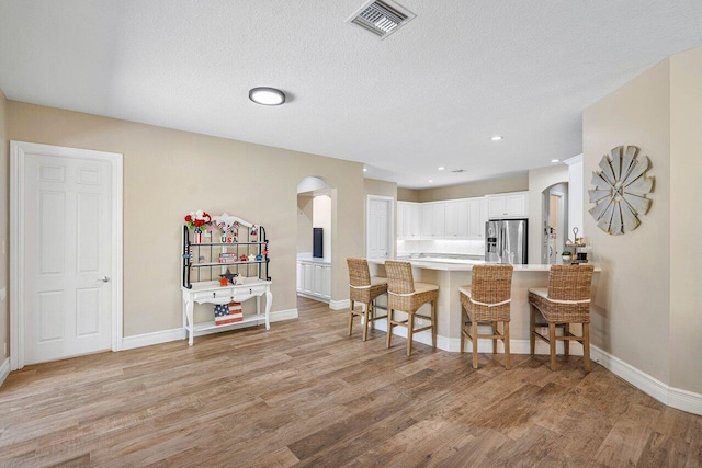 kitchen featuring white cabinetry, light hardwood / wood-style floors, stainless steel fridge with ice dispenser, kitchen peninsula, and a breakfast bar