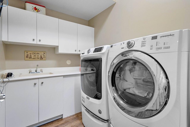 laundry room featuring sink, independent washer and dryer, light hardwood / wood-style floors, and cabinets