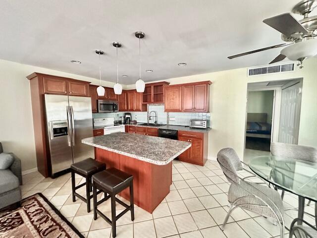 kitchen with decorative light fixtures, a kitchen island, a kitchen bar, appliances with stainless steel finishes, and light tile patterned floors