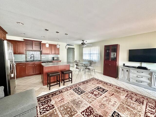 kitchen featuring light tile patterned floors, a kitchen bar, backsplash, stainless steel refrigerator, and a kitchen island