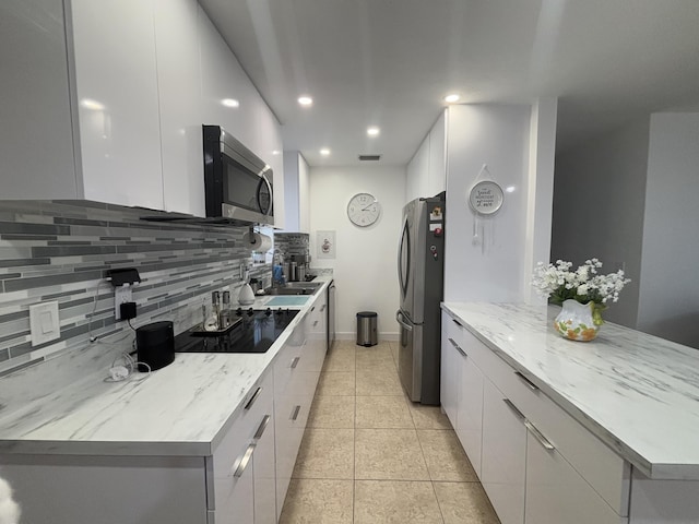 kitchen with white cabinets, stainless steel appliances, backsplash, light stone counters, and light tile patterned floors