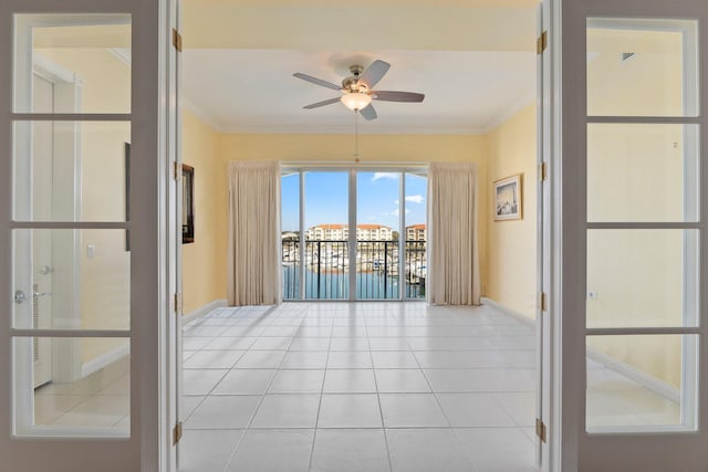 tiled spare room with ornamental molding, ceiling fan, and a water view