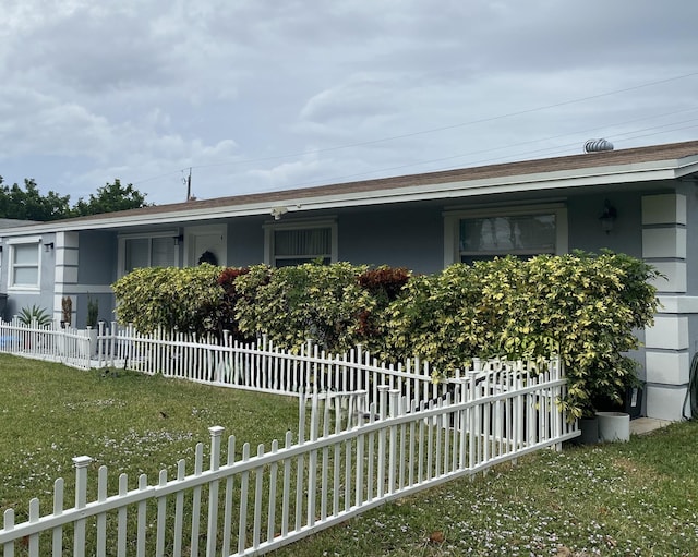 view of side of home featuring a shingled roof, a yard, a fenced front yard, and stucco siding