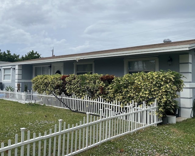 view of side of property with a fenced front yard, roof with shingles, a lawn, and stucco siding