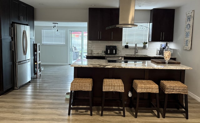 kitchen with tasteful backsplash, light stone countertops, a breakfast bar, freestanding refrigerator, and island range hood