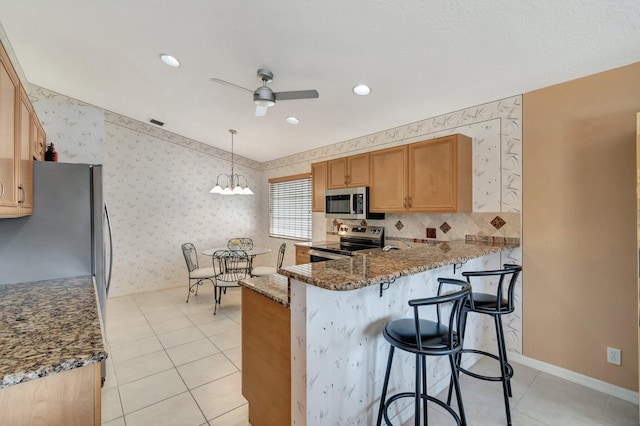 kitchen featuring decorative light fixtures, dark stone countertops, ceiling fan, kitchen peninsula, and stainless steel appliances