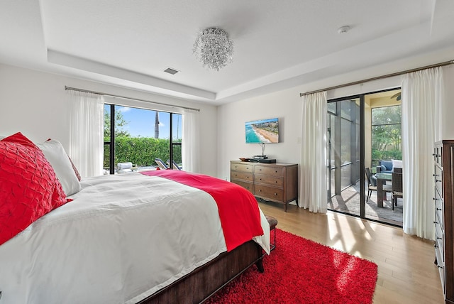 bedroom with light hardwood / wood-style flooring, access to outside, and a tray ceiling