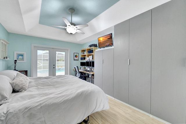 bedroom featuring hardwood / wood-style flooring, access to exterior, french doors, ceiling fan, and a tray ceiling