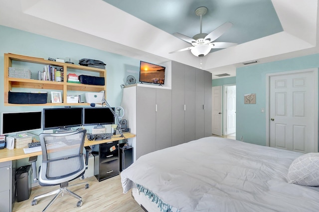 bedroom with ceiling fan, a tray ceiling, and light wood-type flooring