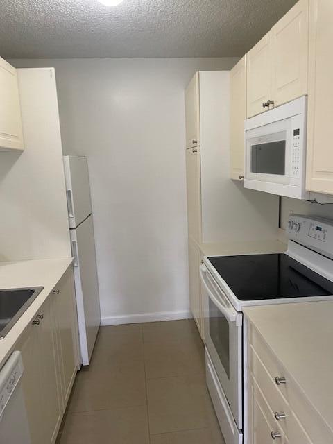 kitchen featuring a textured ceiling, light tile patterned flooring, white cabinets, and white appliances