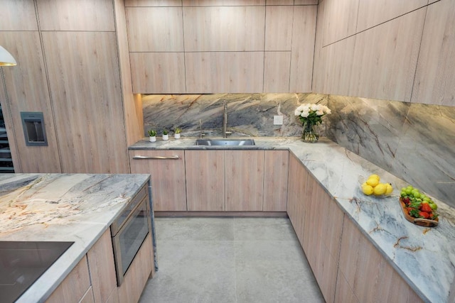 kitchen with stainless steel microwave, light brown cabinetry, light stone countertops, black electric stovetop, and sink