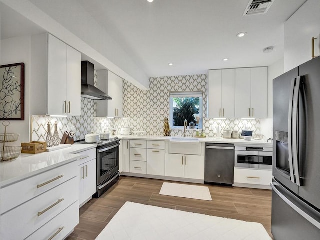 kitchen featuring backsplash, white cabinetry, appliances with stainless steel finishes, and wall chimney exhaust hood