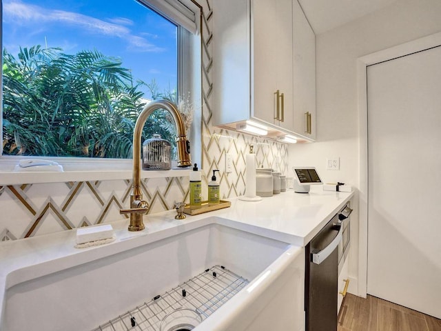 interior space featuring tasteful backsplash, dishwasher, hardwood / wood-style floors, sink, and white cabinets