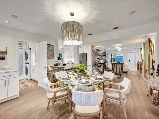 dining space with stacked washing maching and dryer, a chandelier, and light wood-type flooring