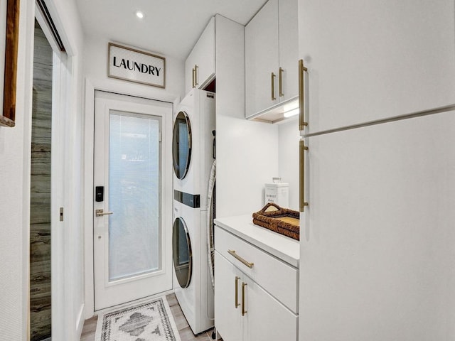 washroom featuring stacked washer and dryer, cabinets, and light hardwood / wood-style flooring