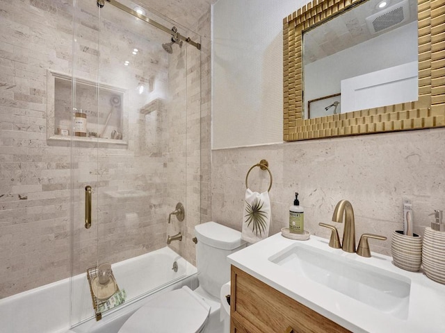 full bathroom featuring tile walls, combined bath / shower with glass door, vanity, and toilet