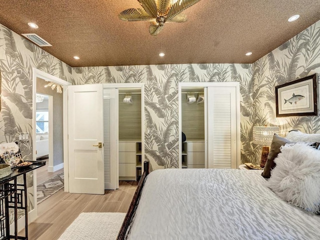 bedroom featuring light wood-type flooring, multiple closets, and ceiling fan