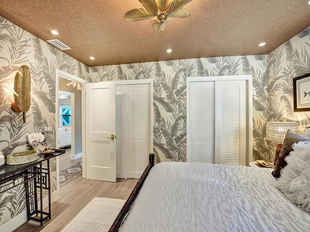 bedroom with a textured ceiling, multiple closets, light hardwood / wood-style flooring, and ceiling fan