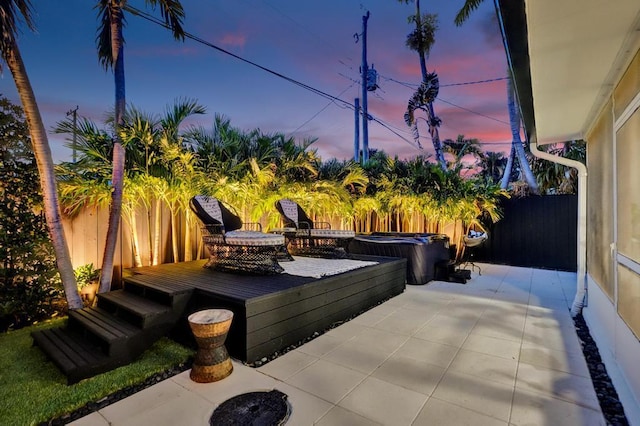 patio terrace at dusk featuring a deck and a hot tub