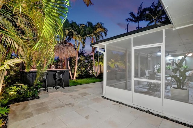 patio terrace at dusk featuring an outdoor bar and a sunroom