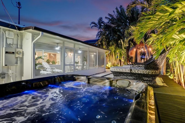 deck at dusk featuring a hot tub and a sunroom