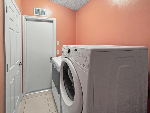 laundry area with light tile patterned flooring, a textured ceiling, and washer and clothes dryer