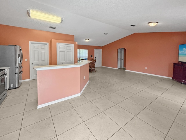 kitchen featuring a kitchen island, light tile patterned flooring, lofted ceiling, and stainless steel refrigerator