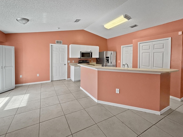 kitchen with vaulted ceiling, white cabinetry, stainless steel appliances, a center island with sink, and light tile patterned flooring