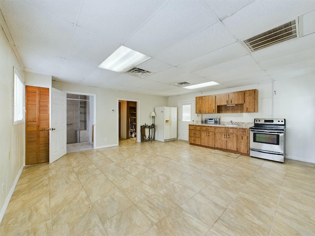 kitchen featuring sink, white fridge with ice dispenser, a drop ceiling, and stainless steel range with electric stovetop