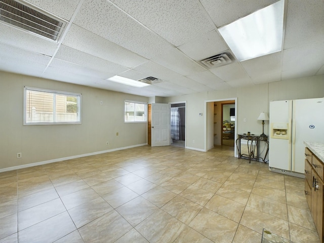 basement featuring white fridge with ice dispenser and a drop ceiling