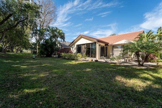 back of house featuring a tiled roof, a sunroom, a lawn, and stucco siding