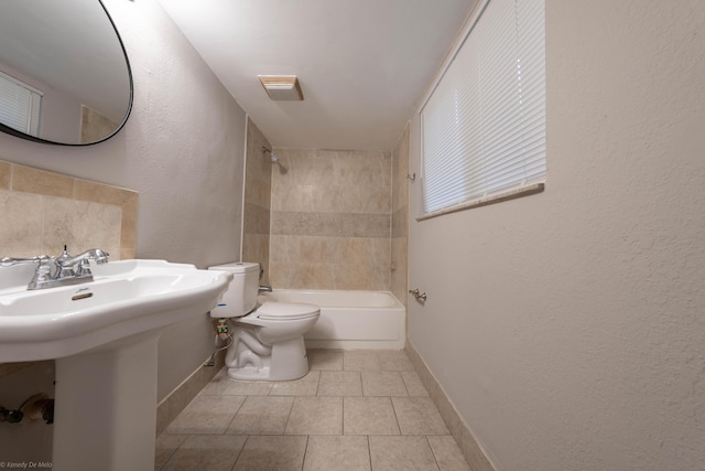 bathroom featuring toilet, tiled shower / bath, and tile patterned flooring