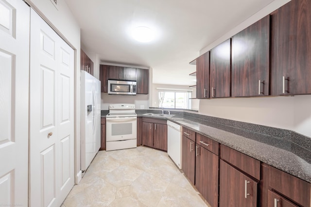 kitchen featuring sink, white appliances, dark brown cabinetry, and dark stone countertops