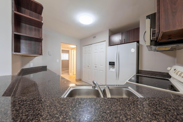 kitchen featuring sink, dark brown cabinetry, dark stone counters, and white appliances