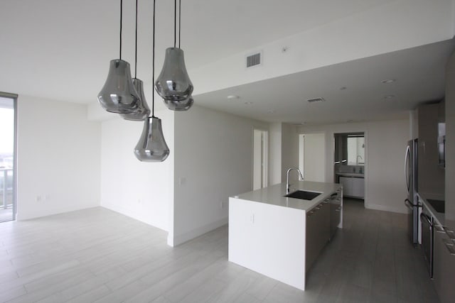 kitchen with stainless steel fridge, sink, decorative light fixtures, hardwood / wood-style flooring, and a center island with sink