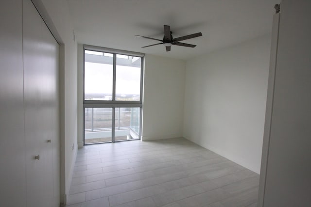 empty room featuring ceiling fan, a wall of windows, and light wood-type flooring