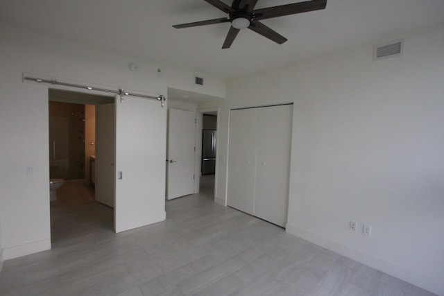 unfurnished bedroom with ceiling fan, a closet, ensuite bath, and a barn door