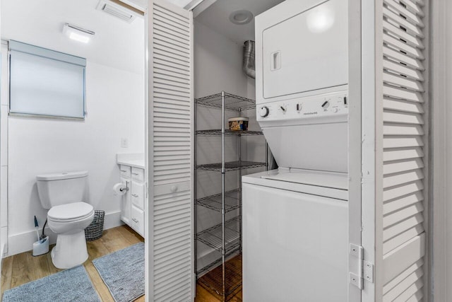 laundry room with hardwood / wood-style flooring and stacked washer / drying machine