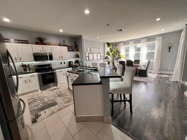 kitchen with appliances with stainless steel finishes, a breakfast bar, white cabinetry, sink, and a kitchen island with sink