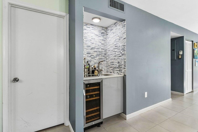 bar featuring sink, tasteful backsplash, light tile patterned floors, and beverage cooler