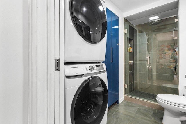 laundry area with dark tile patterned flooring and stacked washing maching and dryer